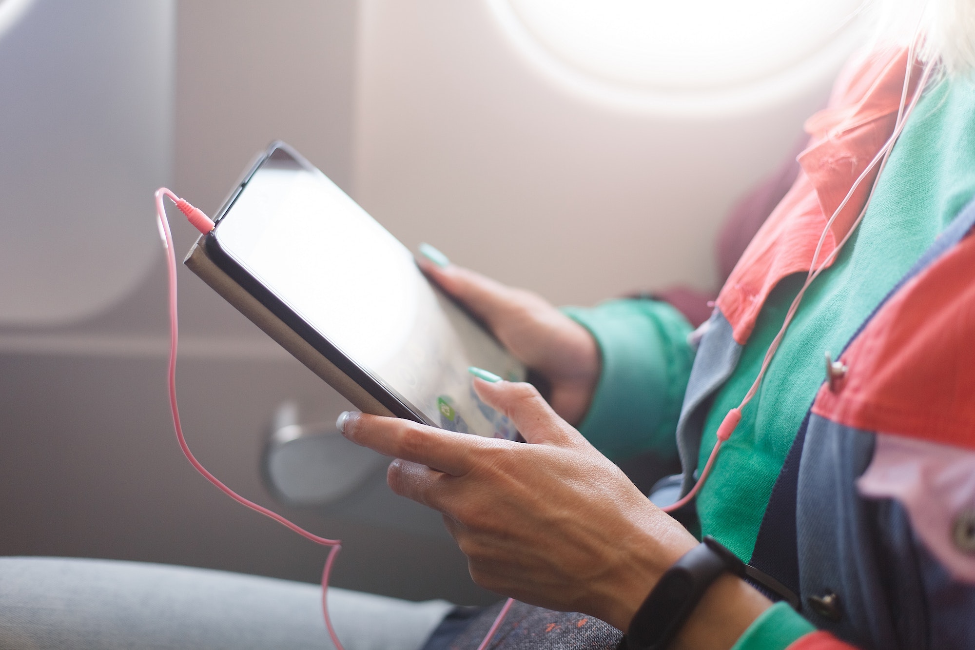 A young woman uses a tablet on the plane. Reading an e-book while traveling. Airplane passenger.