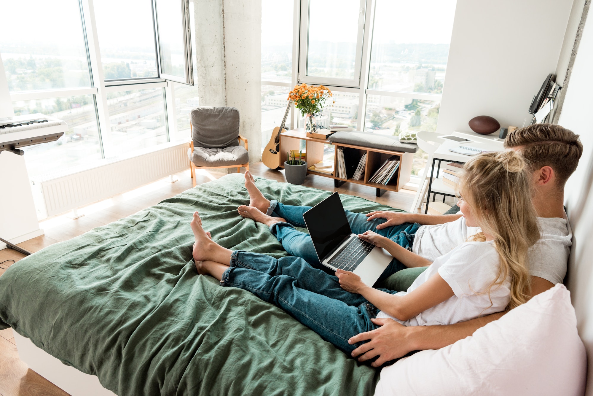 side view of young couple with digital laptop with blank screen resting on bed at home