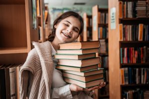 teen girl in the library. Education at school or university. A stack of books in hands.