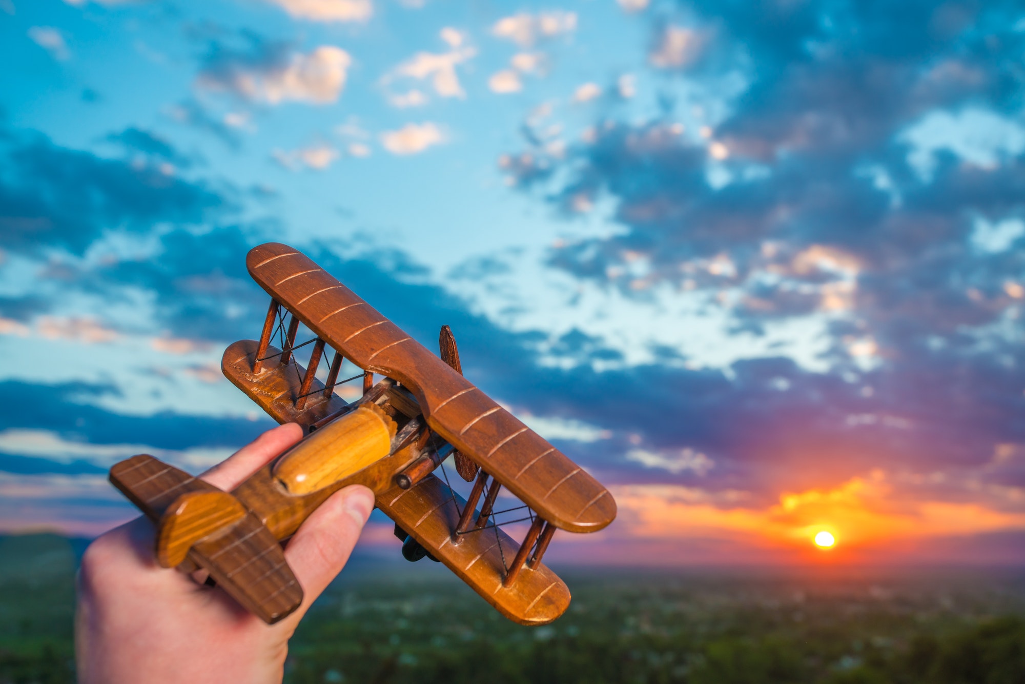 The hand with a toy plane against the background of a sunset